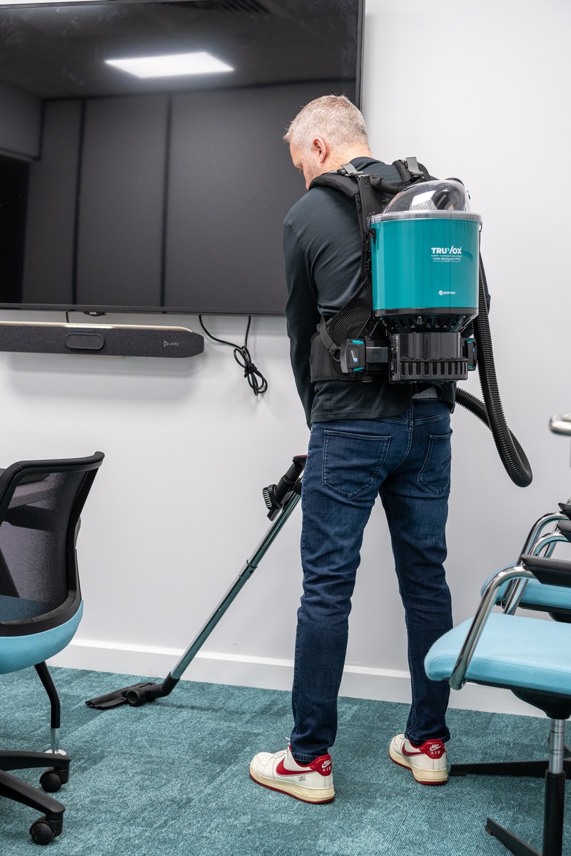 Cleaning operative wearing a Truvox Valet Backpack Pro vacuuming the carpet of a corporate meeting room