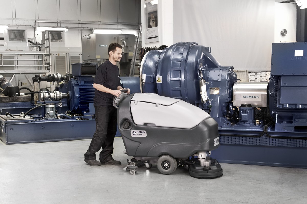 Operator with a Nilfisk SC800 walk-behind scrubber dryer cleaning beside Siemens turbine equipment in a power generation hall