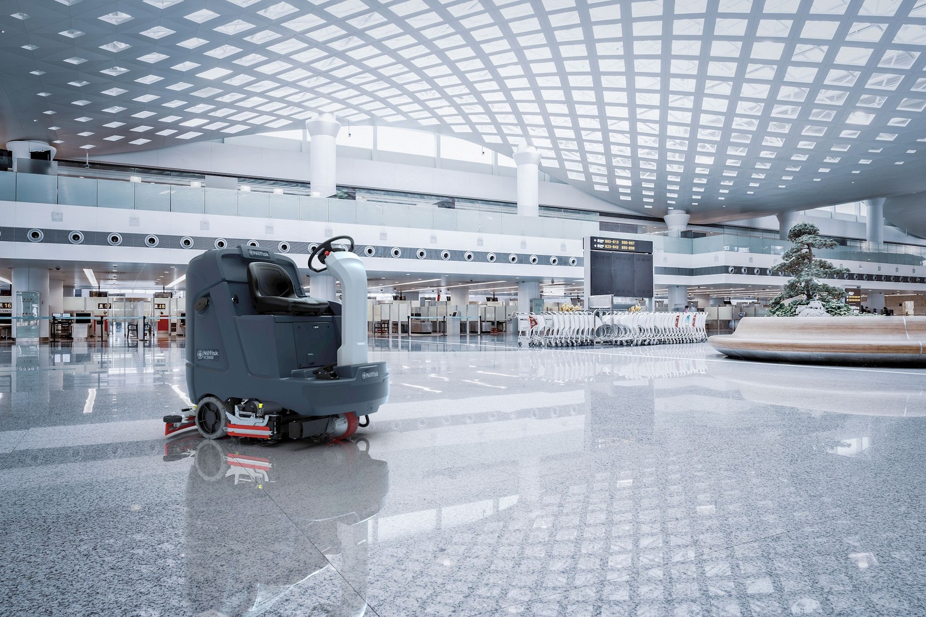 Nilfisk SC5000 ride-on scrubber dryer cleaning a polished granite floor in a vast airport terminal beneath a vaulted glazed ceiling, baggage trolleys and check-in desks in the background