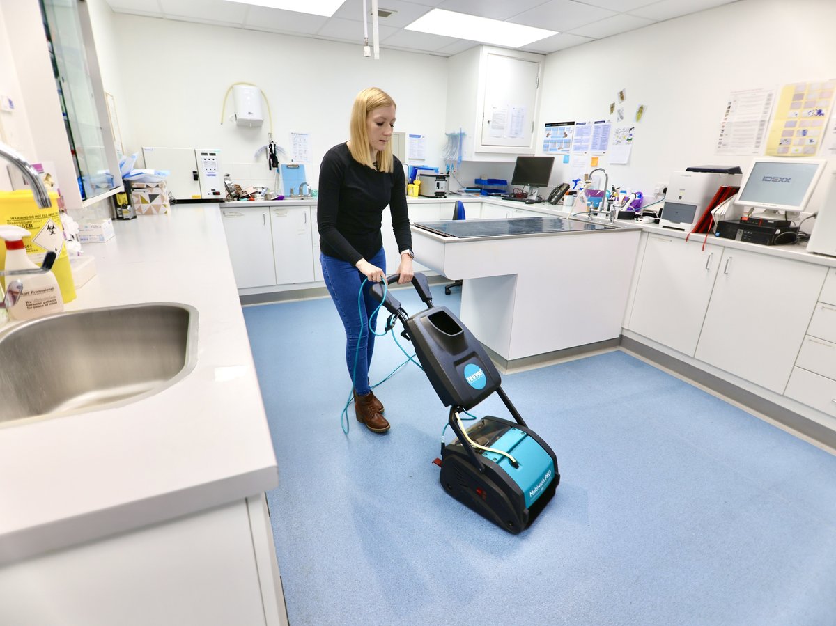A small black dog sitting calmly beside the Truvox Multiwash PRO 240 in a veterinary practice retail area